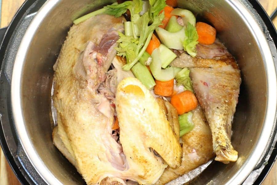 A top down view of an instant pot with a seared chicken carcass and carrots and celery inside.