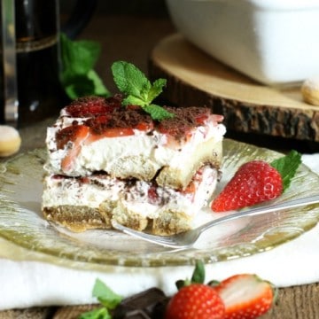 A square piece of strawberry tiramisu in a glass plate, sitting on a white napkin.