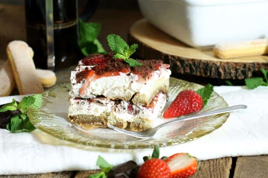 A square piece of strawberry tiramisu in a glass plate, sitting on a white napkin.