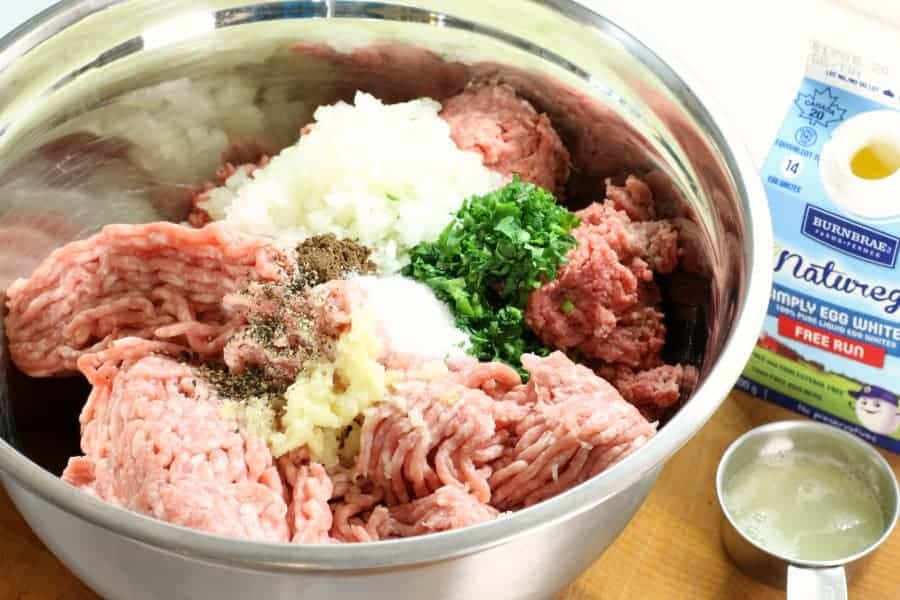 A metal bowl filled with ground prok, ground beef, chopped onion, and spices. The mixture for this swedish meatball recipe