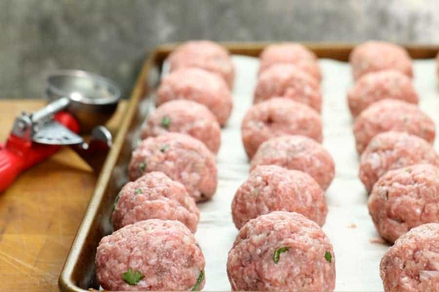 freshly formed swedish meatballs on a parchment lines sheetpan
