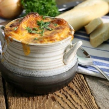 A grey stoneware bowl filled with french onion soup and topped with golden baked cheese.