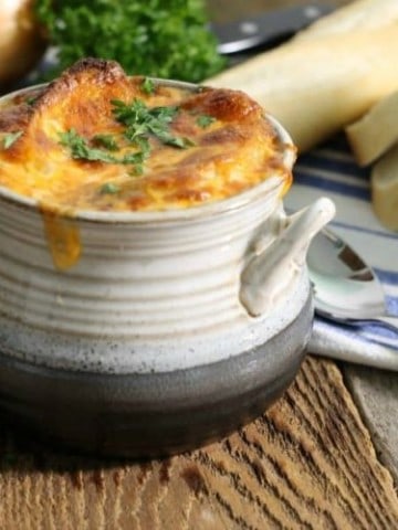A grey stoneware bowl filled with french onion soup and topped with golden baked cheese.
