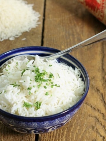 a blue bowl on a barn board tabletop filled with cooked basmati rice