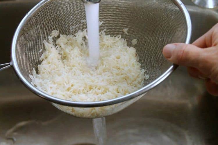 basmati rice being rinsed in a sieve under running water