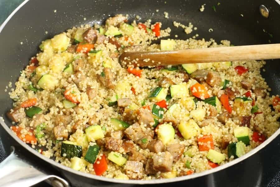 A quinoa and sausage stuffing being mixed in a large frying pan