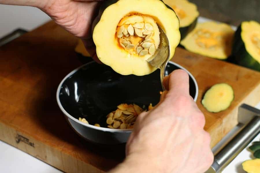 Someone scooping out the seeds of a halved acorn squash