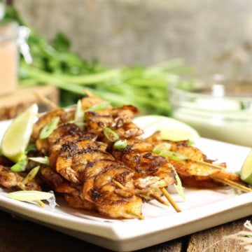 blackened shrimp skewers on a white platter surrounded by dip and various ingredients