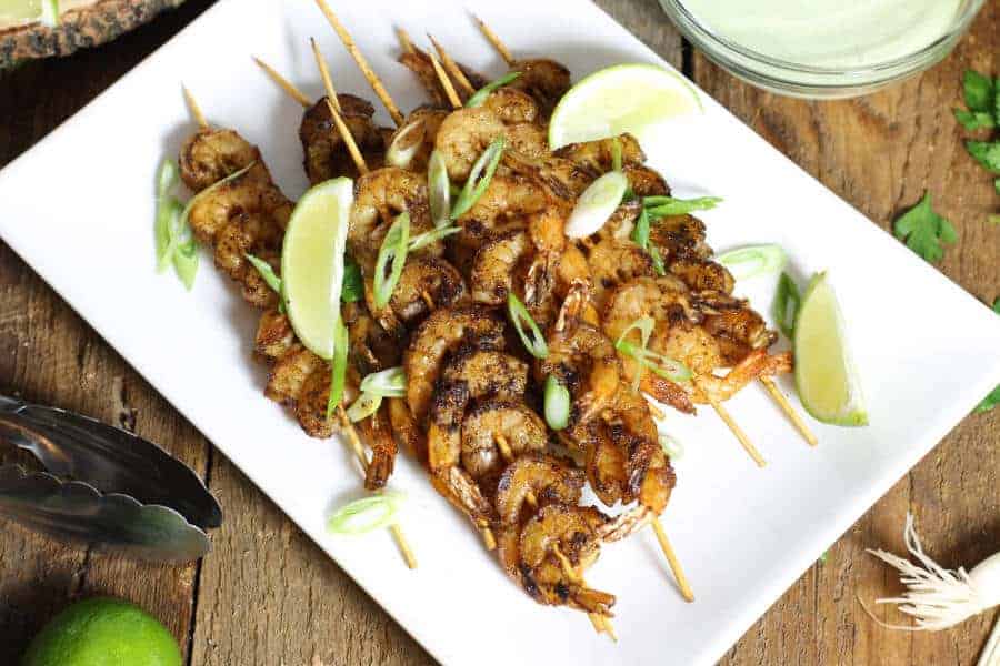 blackened shrimp skewers on a white platter with various garnishes