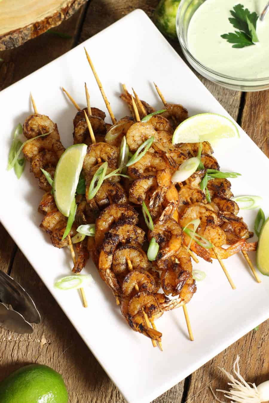 blackened shrimp skewers on a white platter garnished with lime wedges and green onion