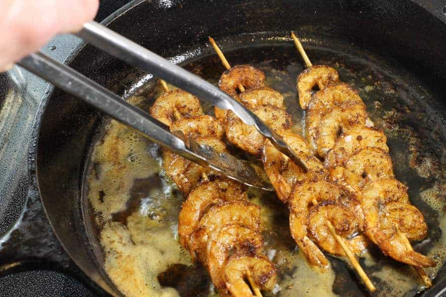 blackened shrimp skewers being flipped in a cast iron skillet while cooking