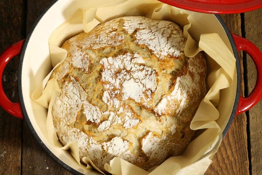 A loaf of freshly baked no knead sourdough bread in a red enamel dutch oven