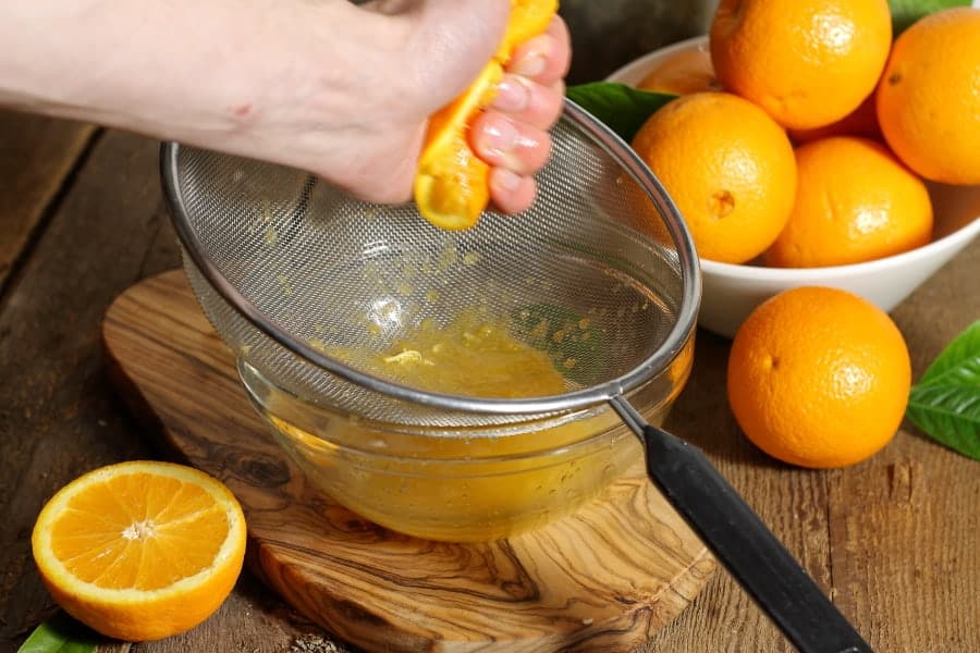 an orange being squeezed over a sieve to make fresh squeezed orange juice.