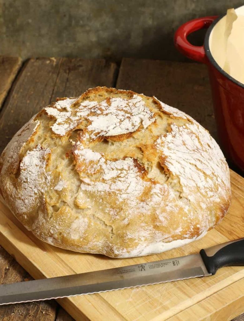 A rustic loaf of homemade no knead sourdough bread on a wooden cutting board