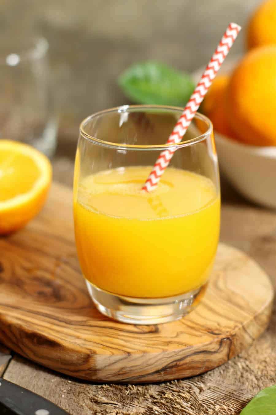 A glass of homemade, fresh squeezed orange juice on a wooden serving board.