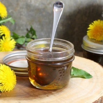 a small mason jar filled with homemade dandelion syrup surrounded by dandelions