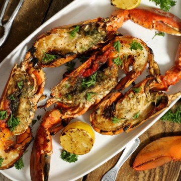 four grilled lobsters garnished with fresh herbs on a white platter