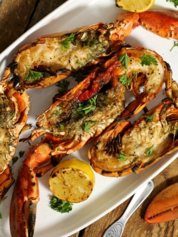 four grilled lobsters garnished with fresh herbs on a white platter