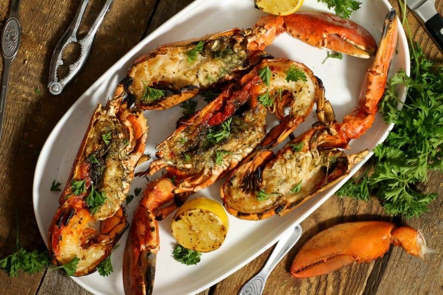 four grilled lobsters garnished with fresh herbs on a white platter