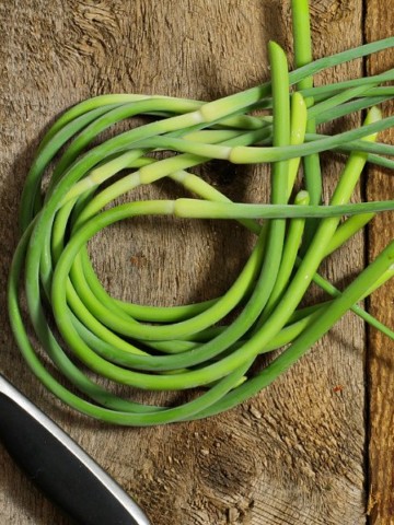 A bunch of freshly harvested garlic scapes on a wooden table top