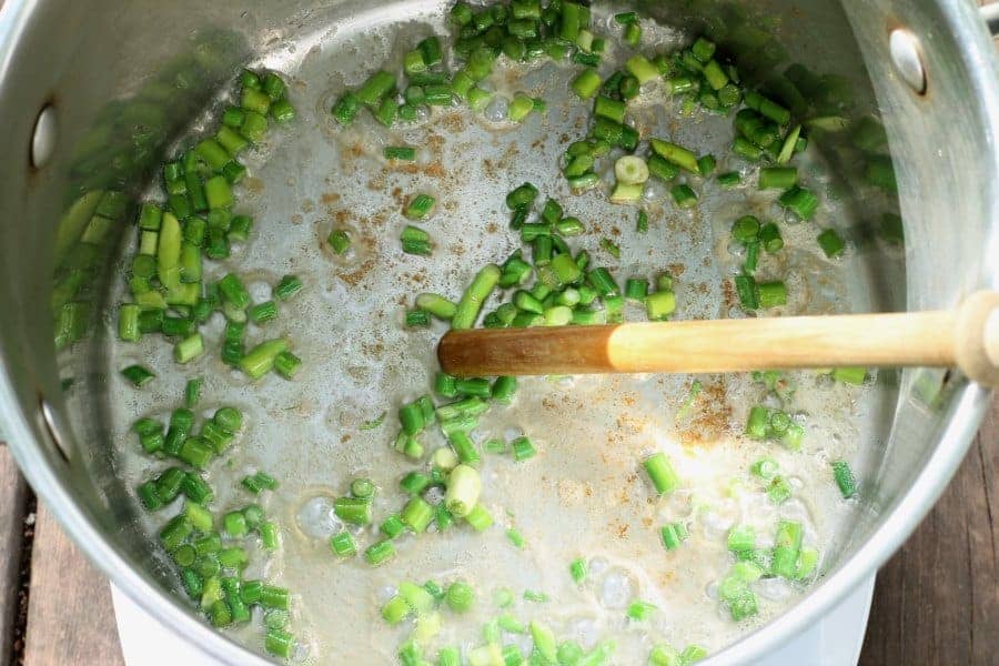 Garlic scapes being sauteed in a pot with butter