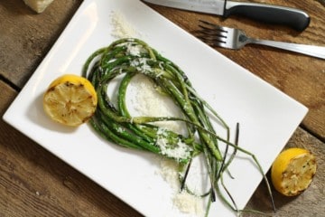 Grilled garlic scapes with grilled lemon and parmesan on a white plate