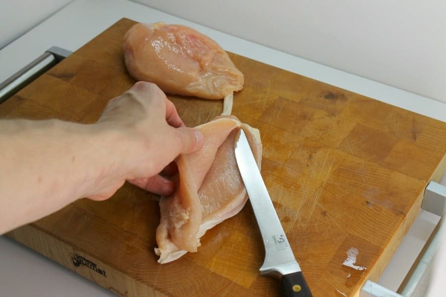 A chicken breast being cut in half for chicken burgers