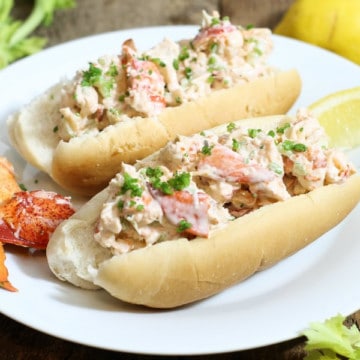 traditional east coast lobster rolls on a plate garnished with chives and lemon