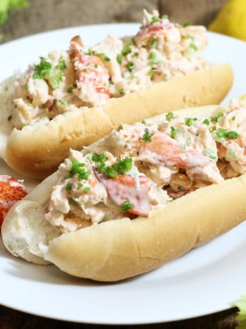 traditional east coast lobster rolls on a plate garnished with chives and lemon