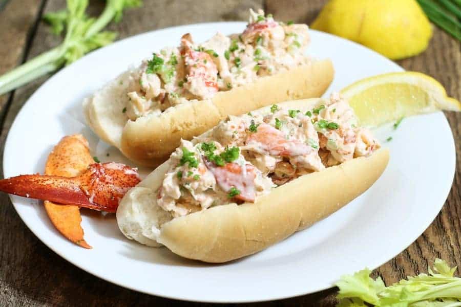 traditional east coast lobster rolls on a plate garnished with chives and lemon