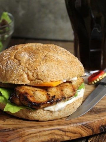 a fully assembled marinated grilled chicken burgermon a wooden serving board