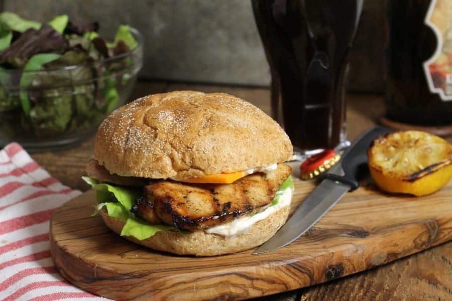 a fully assembled marinated grilled chicken burger on a wooden serving board
