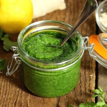 Toasted almond and arugula pesto in a mason jar surrounded by various ingredients