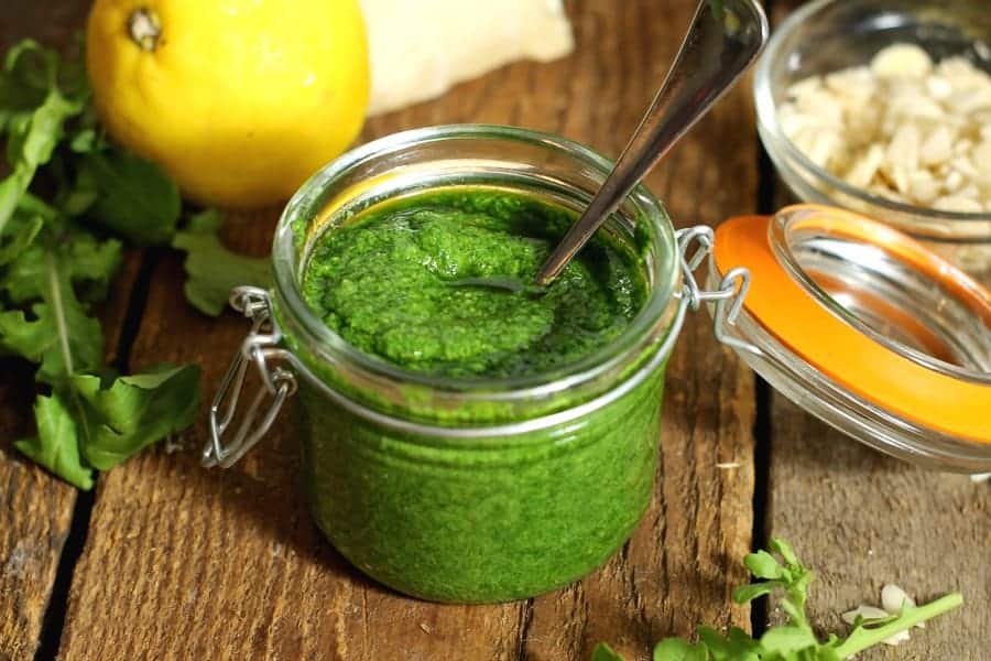 Toasted almond and arugula pesto in a mason jar surrounded by various ingredients