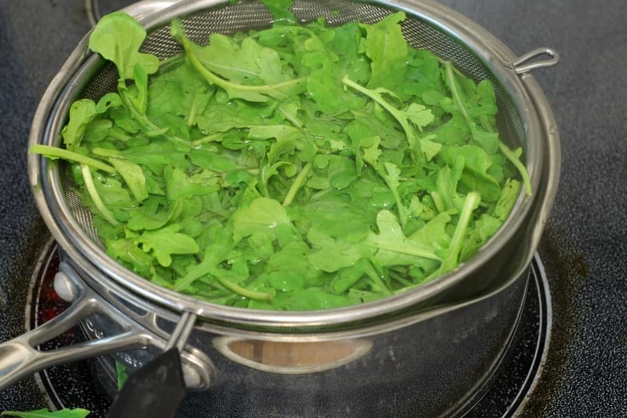 raw arugula being blanched in a pot of boiling water