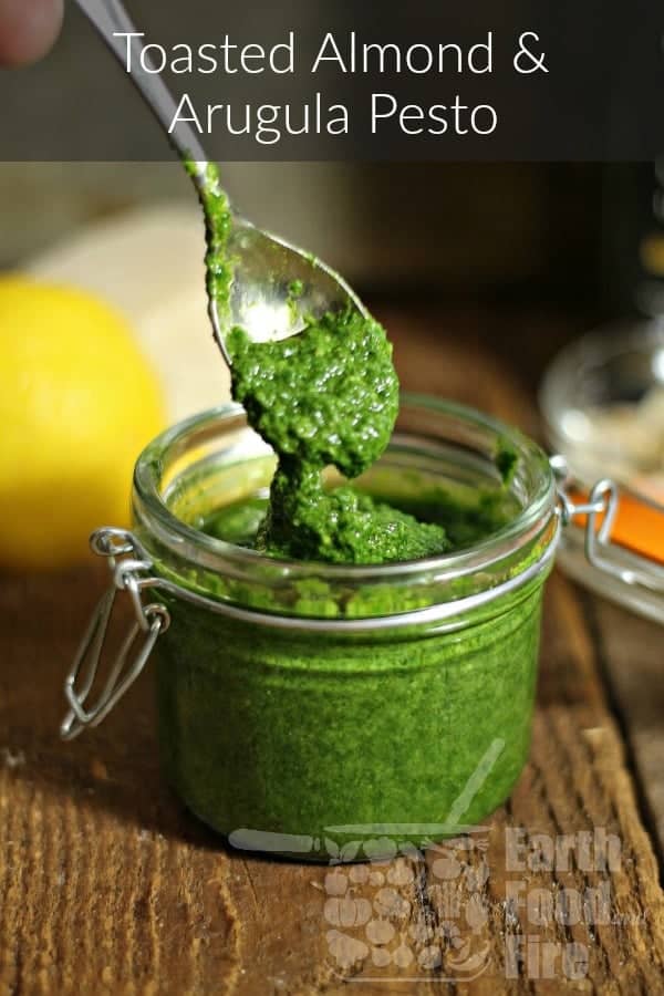 Toasted almond and arugula pesto being spooned into a small mason jar.