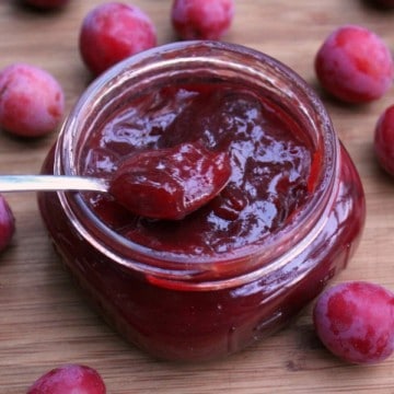 a jar of homemade wild plum jam surrounded by the wild foraged fruits on a wooden surface