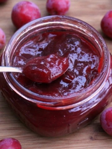 a jar of homemade wild plum jam surrounded by the wild foraged fruits on a wooden surface