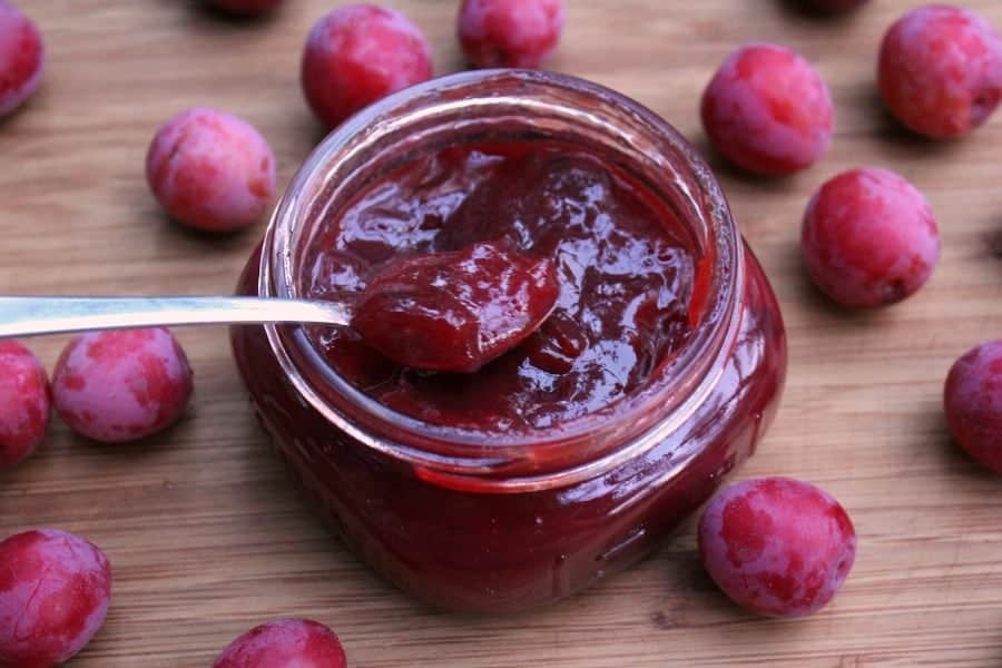 a jar of homemade wild plum jam surrounded by the wild foraged fruits on a wooden surface