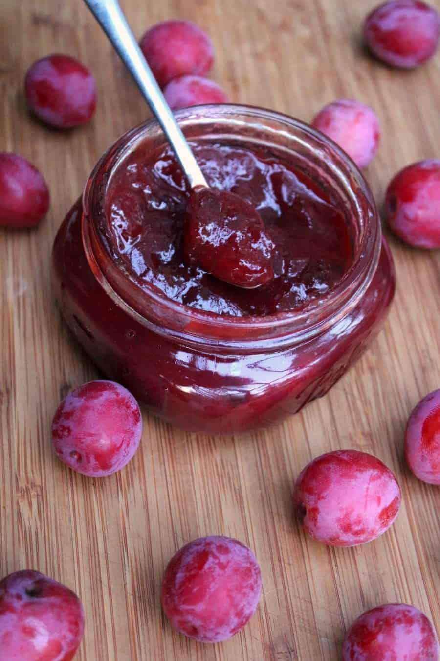 a vertical image of wild plum jam in a small glass jar