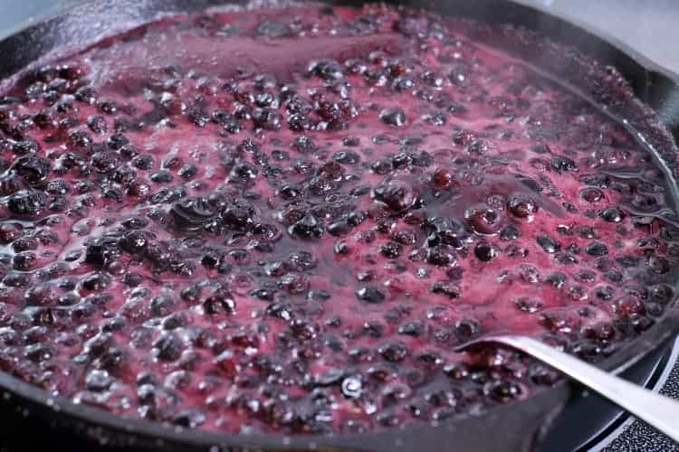 Blueberries, sugar, cinnamon and lemon cooking in a cast iron pan to create a bubbling fruity sauce