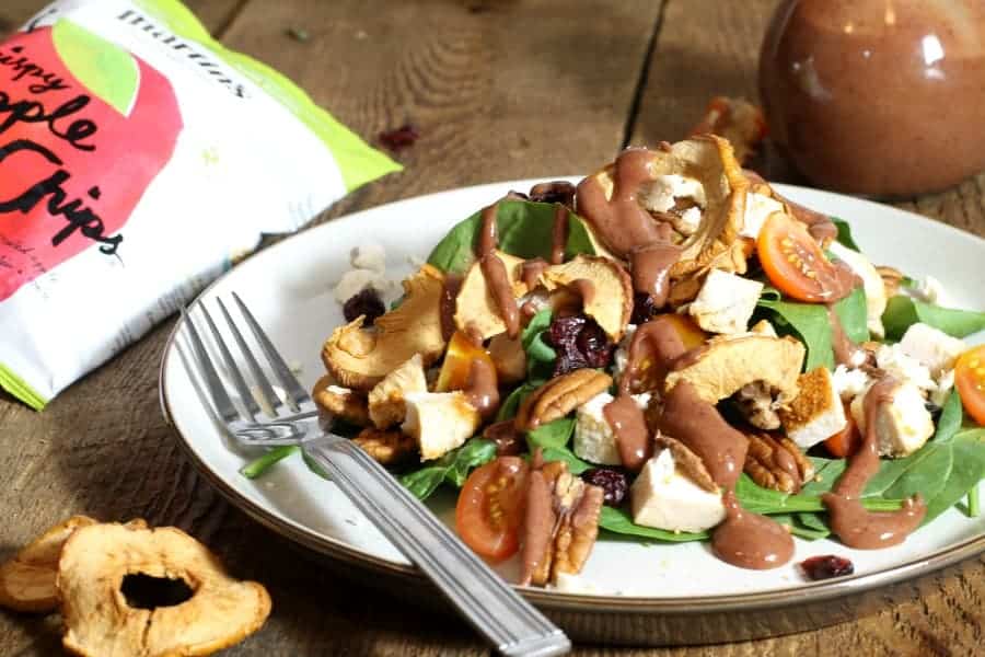 A plate loaded with a chicken spinach salad topped with apple chips, feta, tomato and pecans