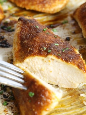 sliced open oven baked chicken breasts on a parchment lined sheet pan
