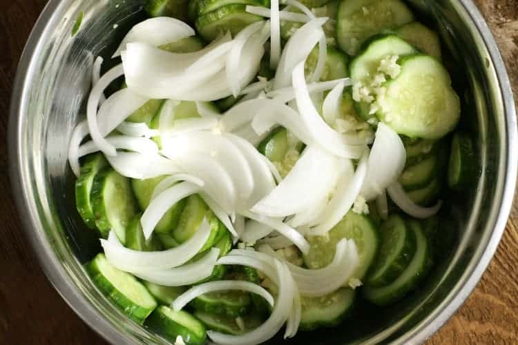 onions and minced garlic being added to the salted cucmbers