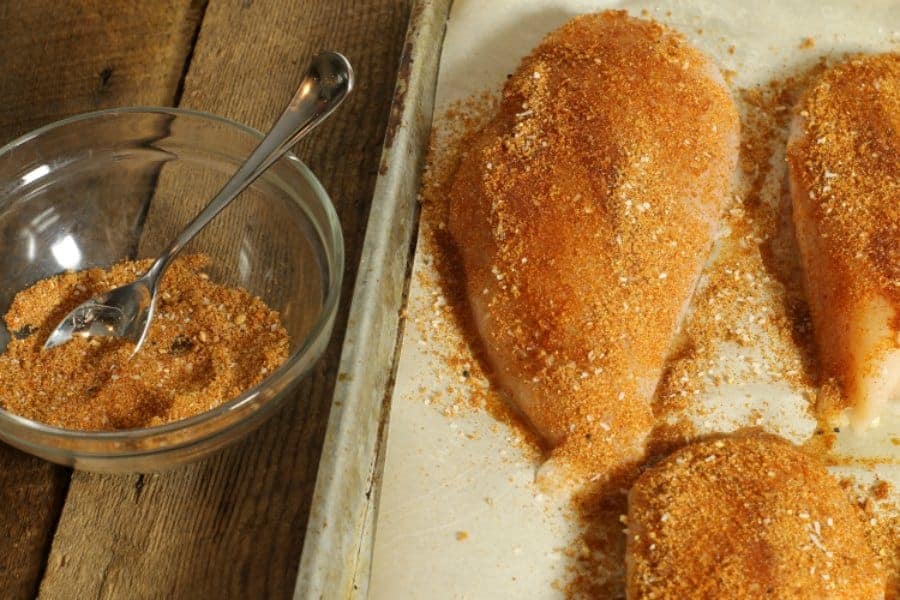 uncooked chicken breasts being covered in homemade chicken seasoning.