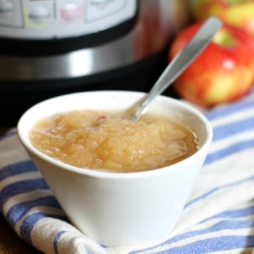 a close up of a white bowl filled with instant pot applesauce on a blue striped dish towel