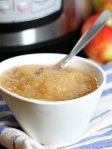 a close up of a white bowl filled with instant pot applesauce on a blue striped dish towel