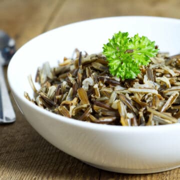 A white bowl filled with cooked wild rice, displayed on a rustic barn board background, and garnished with fresh parsley.