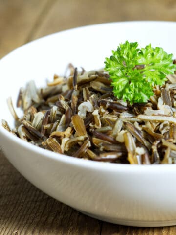 A white bowl filled with cooked wild rice, displayed on a rustic barn board background, and garnished with fresh parsley.