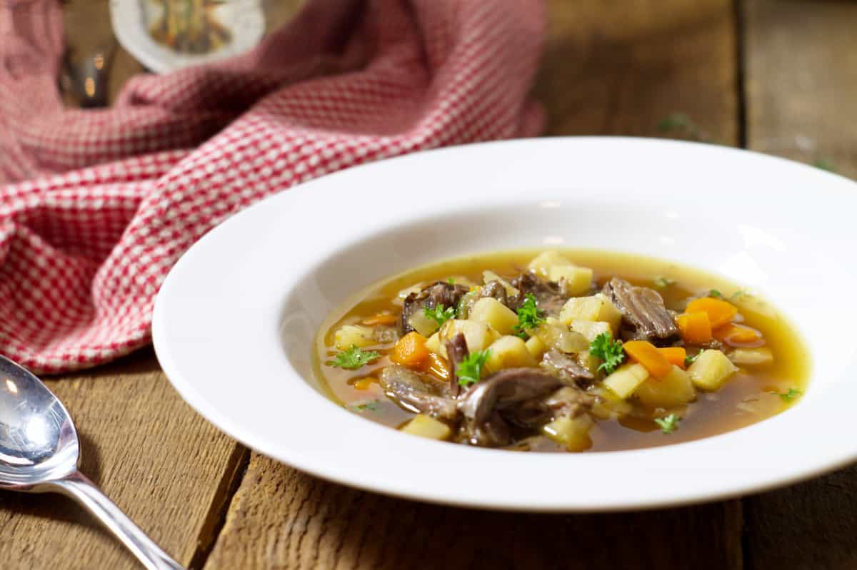 a close up of a white rimmed bowl filled with a broth based oxtail soup